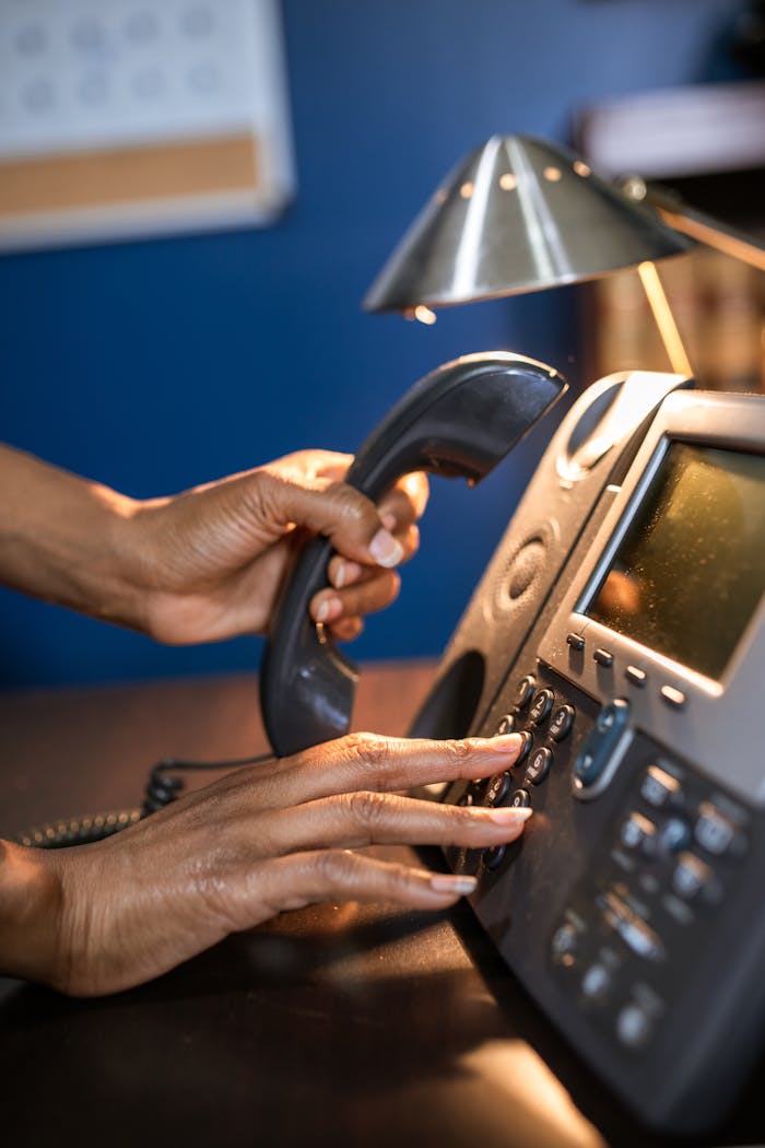 A person dialing a phone call on a desk telephone, focusing on hand details.